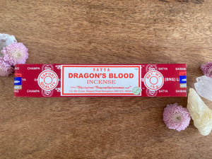 Satya Dragon's Blood incense packaging on a wooden surface with flowers and crystals.