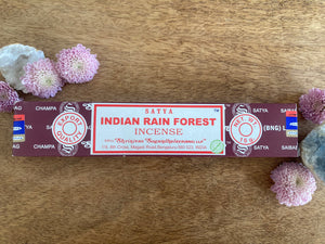 Satya Indian Rain Forest incense packaging on a wooden surface with flowers.