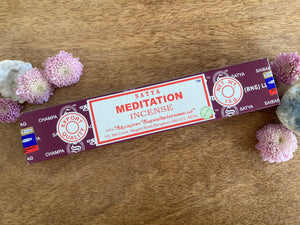 Satya Meditation incense stick box on a wooden surface with flowers around