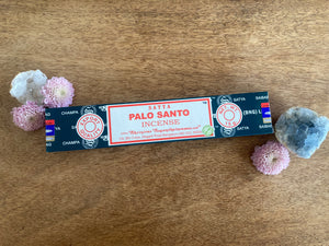 Box of Satya Palo Santo incense on a wooden surface with flowers and a crystal.