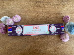 Satya Reiki incense packaging on a wooden surface with flowers and crystals.