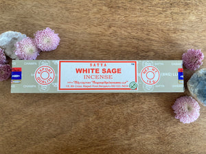 Box of Satya White Sage incense on a wooden surface with flowers and crystals.