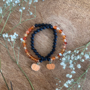 black agate and carnelian bracelet with pumpkin charm with flowers surrounding them on a wooden background