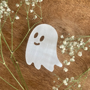 selenite ghost carving on wooden background with flowers around it 