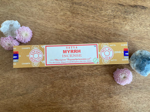 Box of Satya Myrrh incense on a wooden surface with decorative flowers and crystals.
