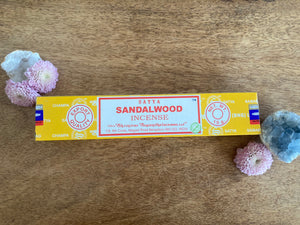 Satya Sandalwood incense box on a wooden surface with decorative flowers and a crystal.